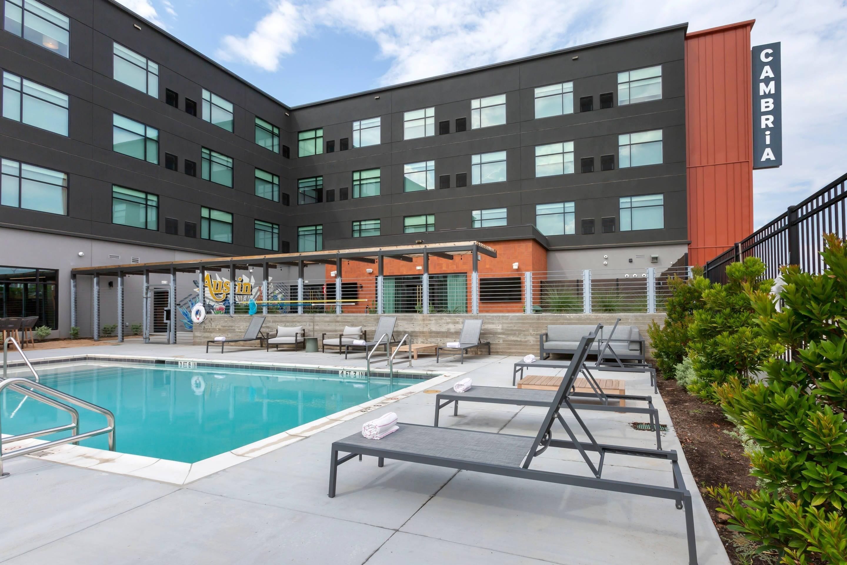 Un edificio moderno con piscina, sillones de descanso y un cartel que dice 'CAMBRIA'.