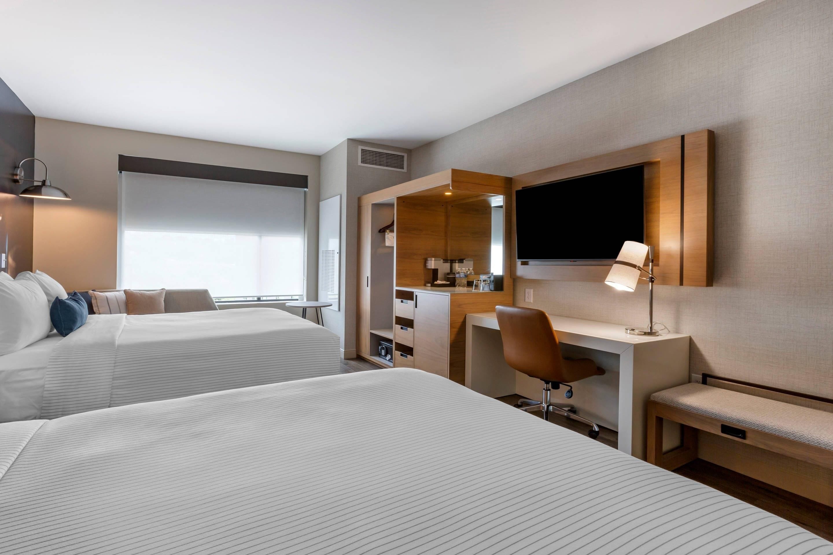Habitació d'hotel amb dos llits, una taula, una cadira, un televisor i una finestra.