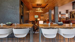 Un interior moderno con techo de madera, zona de bar con taburetes y un área de estar con mesas y sillas.