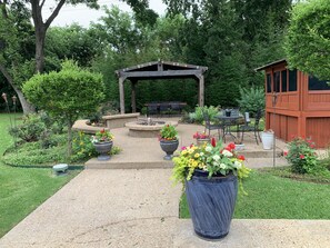 Eine Terrassenfläche mit einer Pergola, Sitzgelegenheiten im Freien und Kübelpflanzen.