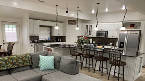 Una cocina moderna con armarios blancos, un sofá seccional gris y un comedor con taburetes de bar.