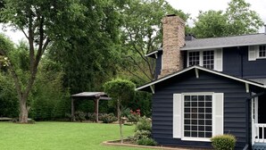 Una casa oscura con chimenea, un árbol pequeño y un césped bien cuidado.