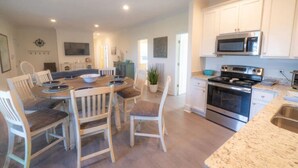 Una cocina moderna con armarios blancos, electrodomésticos de acero inoxidable y una zona de comedor con sillas y una mesa de madera.