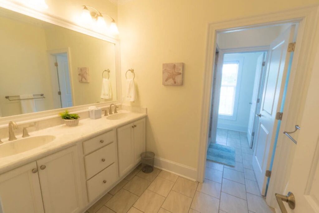 A bathroom with a double sink, a large mirror, and a trash can.