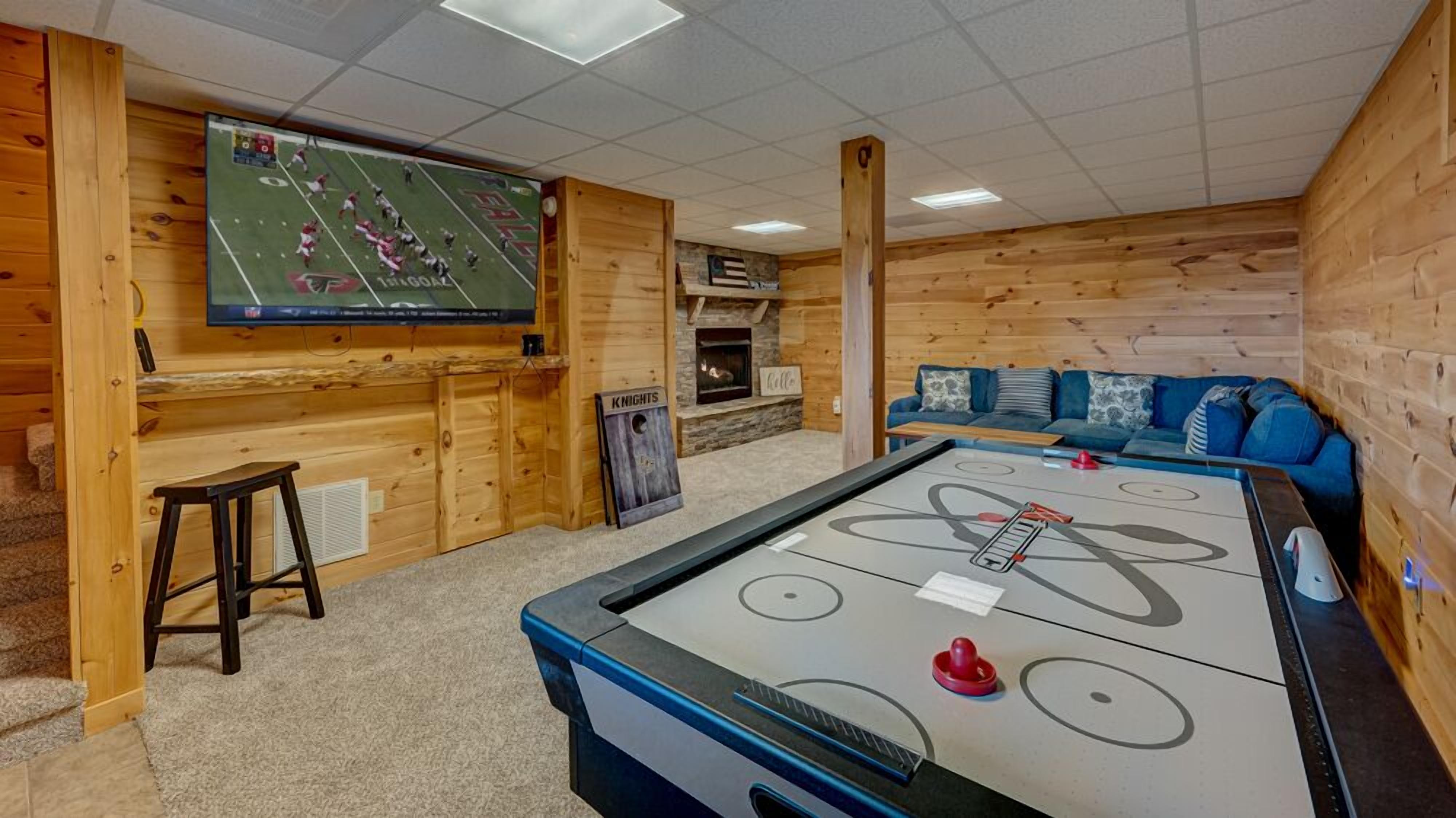A cozy room with a pool table, a television mounted on the wall, and a stone fireplace.