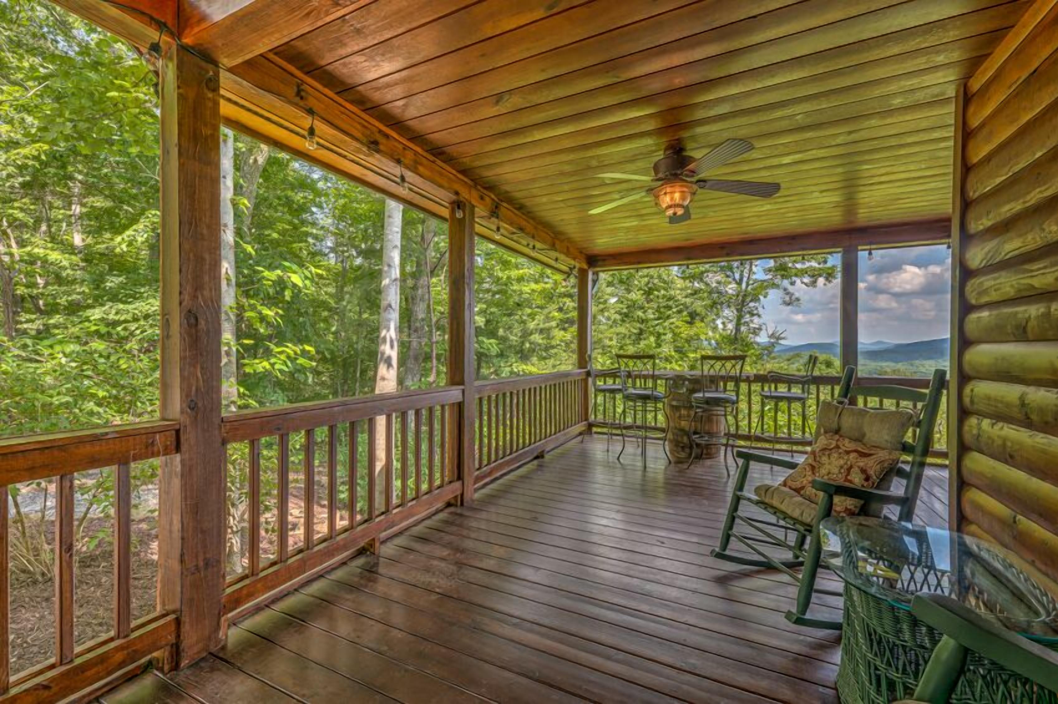 A wooden deck with a ceiling fan, a rocking chair, and a table with chairs.