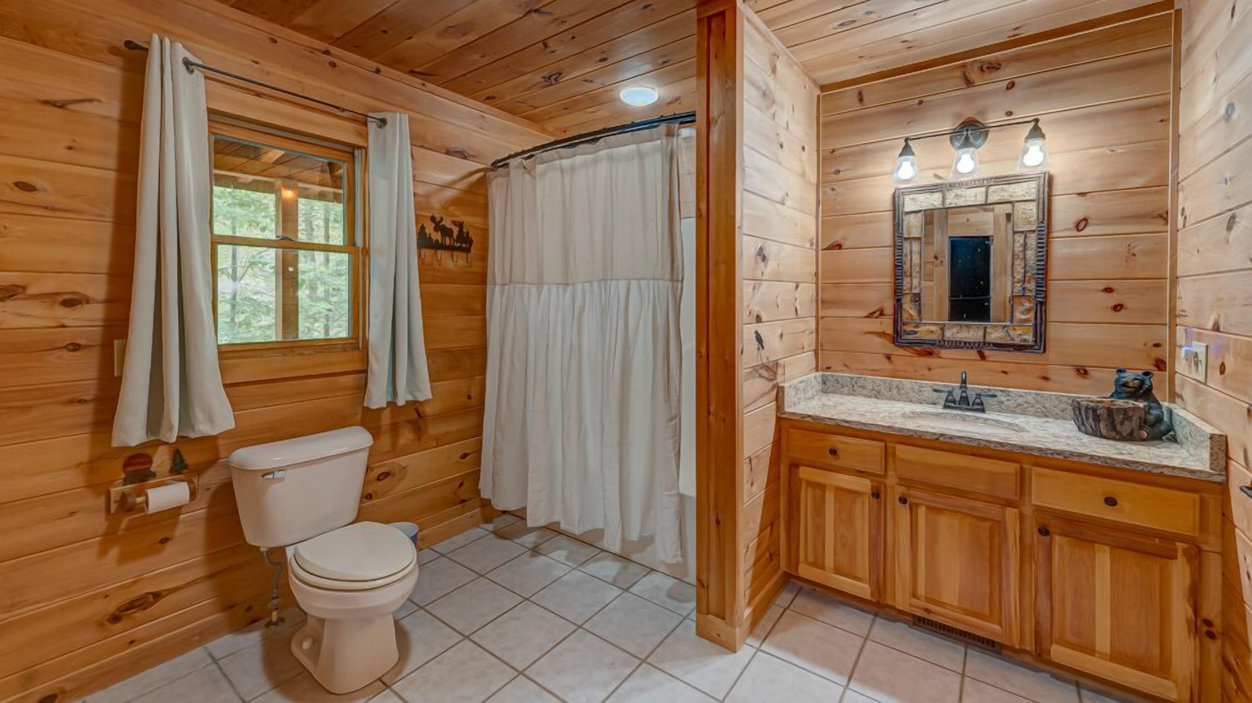 A wooden cabin bathroom with a toilet, shower curtain, sink with a mirror, and a bear decoration.