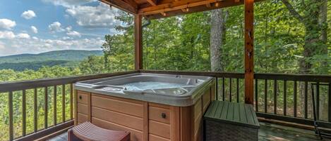 A hot tub on a wooden deck with a view of a forested landscape.