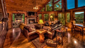 Ein gemütliches Blockhaus-Interieur mit Kamin, Ledersofas und großen Fenstern mit Blick auf den Wald.