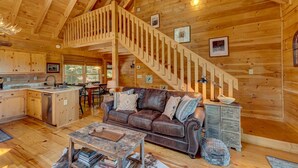 Ein Holzblockhaus-Innenraum mit Essbereich, einem Wohnzimmer mit Ledersofa, einer Treppe und einer Küche.