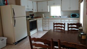 A compact kitchen with white cabinets, a refrigerator, an oven, a microwave, and a dining table with chairs.