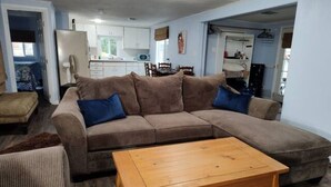A living room with a sectional sofa, a wooden coffee table, and a kitchen in the background.