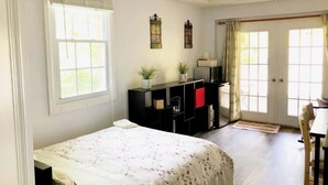 A bedroom with a bed, a desk, and a chair. There are two windows with curtains, a door, and a shelf with decorative items. - Private, Sanitized Loft, with Discounts Sleeps 2 (Lynchburg)