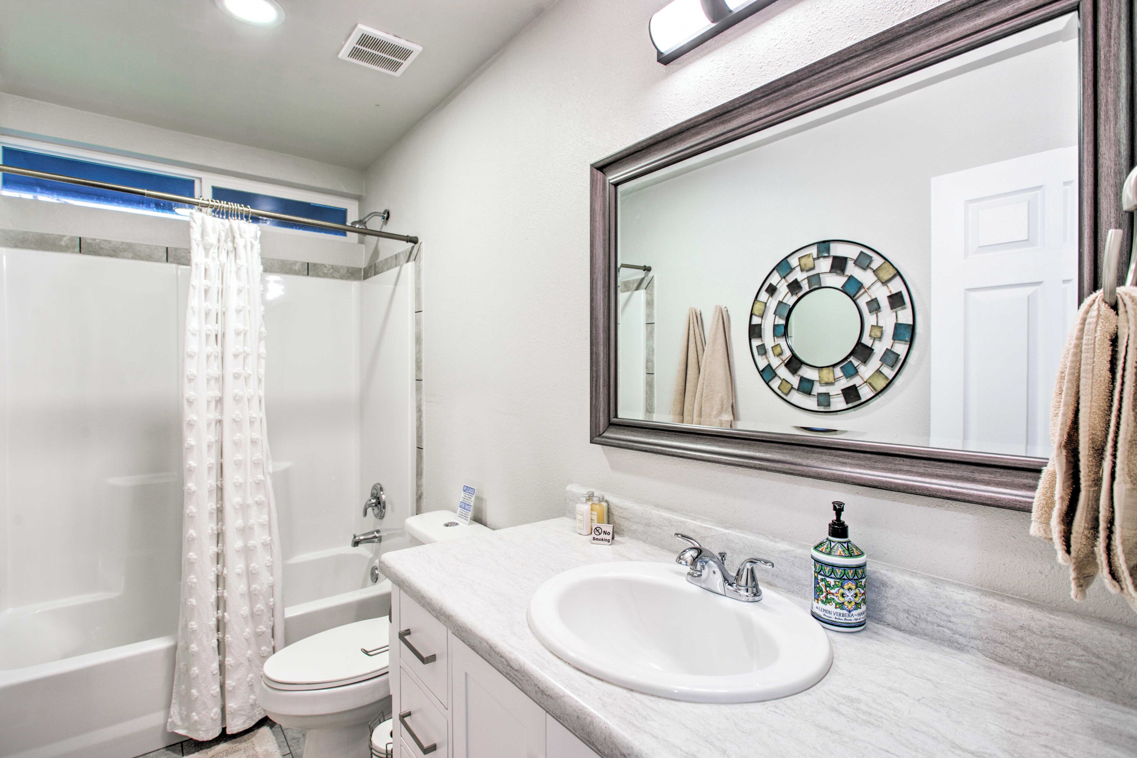 A bathroom with a white sink, a mirror with a decorative frame, a shower curtain, and a towel rack.
