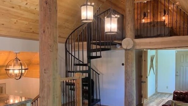 A wooden interior with a spiral staircase, a dining area with a table and chairs, and a hanging light fixture.