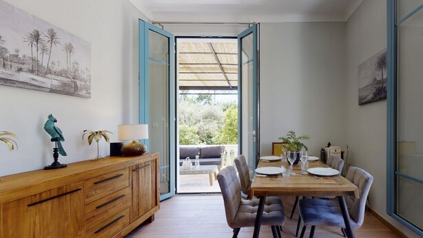 Een eetruimte met een houten tafel, stoelen en uitzicht door een open deur op een terras.
