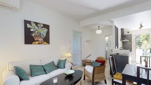 A modern living room with a sofa, coffee table, and wicker chairs. A painting is on the wall, and a kitchen is visible in the background. - Suite Riviera Five stars Holiday house (Beaulieu sur mer)