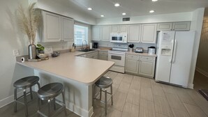A modern kitchen with white cabinets, a central island with bar stools, a microwave, oven, and refrigerator.