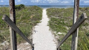 A sandy beach path leading to the ocean, flanked by wooden posts.