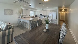 A modern kitchen with white cabinets, a central island, and a dining area with a wooden table and chairs.