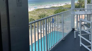 A balcony with a view of the beach, a pool, and a sign indicating the room's location.