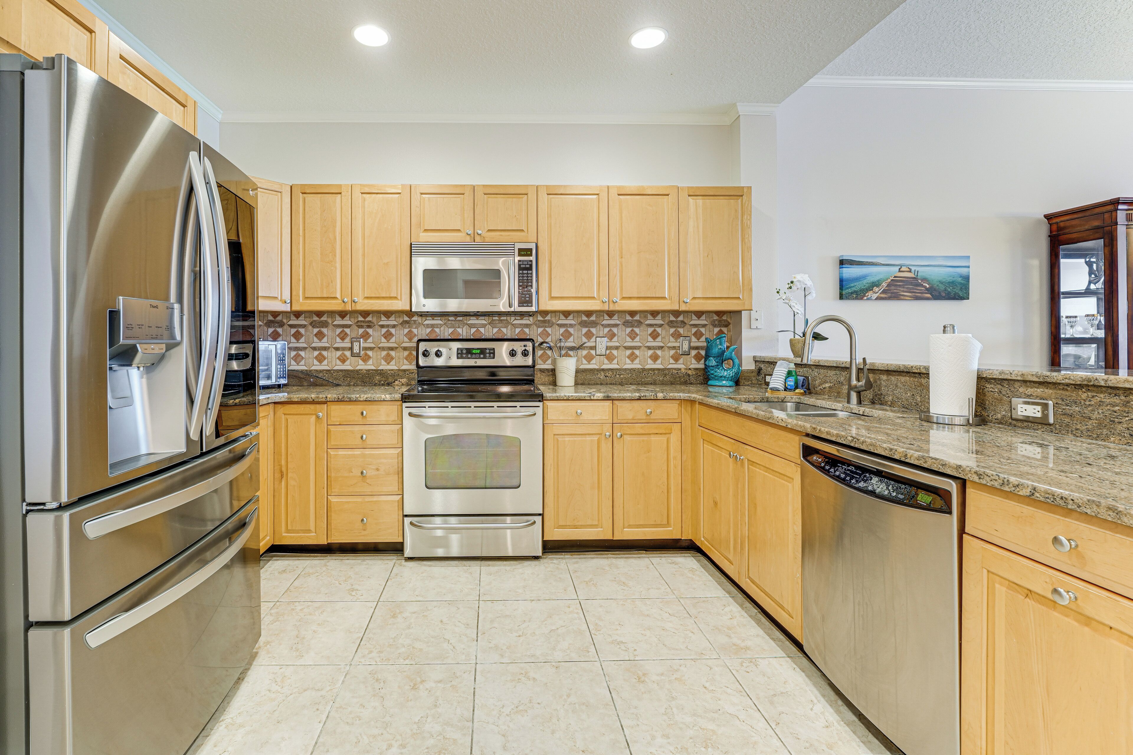 A kitchen with stainless steel appliances, wooden cabinets, a granite countertop, and a painting on the wall.
