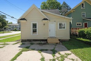 A single-story house with a front porch, a door, and a small set of steps leading to the entrance. - Entire Home I 3 Bedroom I 2 Bath (Lansing)