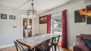Een eetgedeelte met een houten tafel en stoelen, een keuken op de achtergrond en een zithoek met een leren bank.