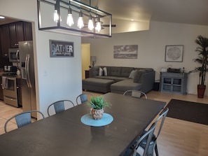 Una cocina moderna con electrodomésticos de acero inoxidable, un comedor con mesa y sillas, un sofá gris y una planta en maceta.
