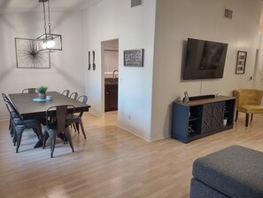 Uma sala moderna com área de jantar, televisão de tela plana na parede e uma poltrona amarela.