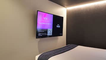 A modern hotel room with a flat-screen TV mounted on the wall displaying a welcome message and QR code instructions for casting.