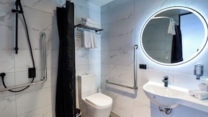 A modern bathroom with a toilet, shower, and sink, equipped with grab bars and a mirror. - The Viv Hotel Wellington (Wellington)