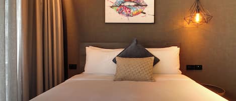 A hotel room with a bed, a pillow, a wall-mounted artwork, and a hanging light fixture.