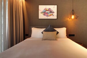 A hotel room with a bed, a pillow, a wall-mounted artwork, and a hanging light fixture.