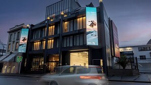 A modern building with large banners advertising ski trips, a visible entrance, and a car passing by.