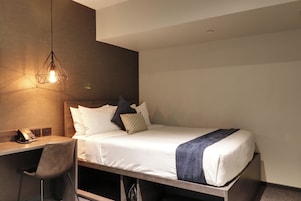 Una camera d'albergo moderna con un letto, una scrivania, una sedia e una lampada a sospensione.