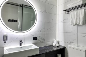 A modern bathroom with a round mirror, white marble tiles, a black countertop, a white sink, and a towel rack. - Microtel by Wyndham Wellington (Wellington)