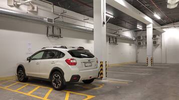 Un SUV blanco estacionado en un estacionamiento subterráneo de varios niveles, con conductos de ventilación y columnas estructurales visibles.