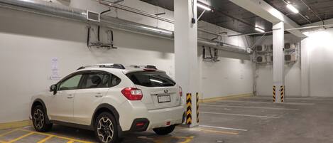 A white SUV parked in a multi-level underground parking garage with visible ventilation ducts and structural columns.