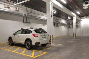 A white SUV parked in a multi-level underground parking garage with visible ventilation ducts and structural columns.