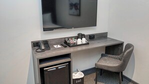 A hotel room with a flat-screen TV mounted on the wall, a desk with a phone, a coffee maker, and a chair.