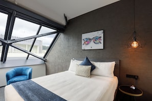 A modern bedroom with a large bed, a blue chair, a wall-mounted artwork, and a hanging light fixture. - The Viv Hotel Wellington (Wellington)