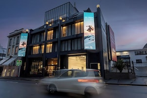 A modern building with large banners advertising ski trips, a visible entrance, and a car passing by.