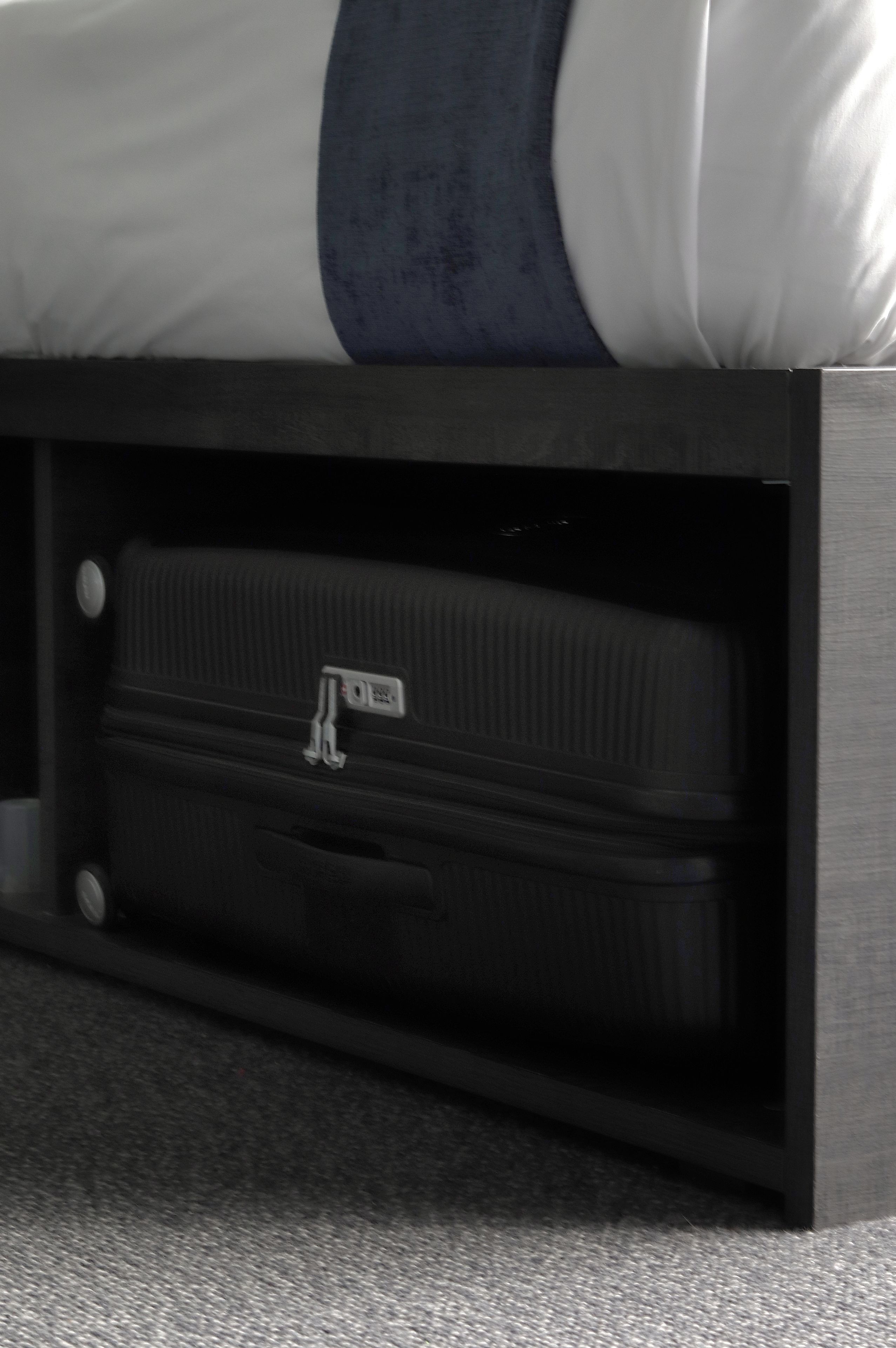 A bed with a dark headboard and a suitcase placed under it.