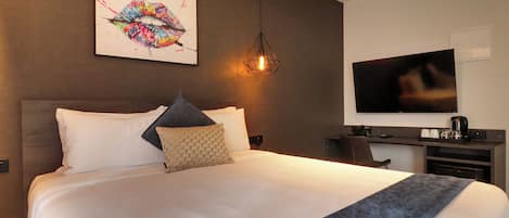 Une chambre d’hôtel moderne dotée d’un grand lit, d’une télévision à écran plat, d’un bureau avec une machine à café et d’une œuvre d’art murale originale.
