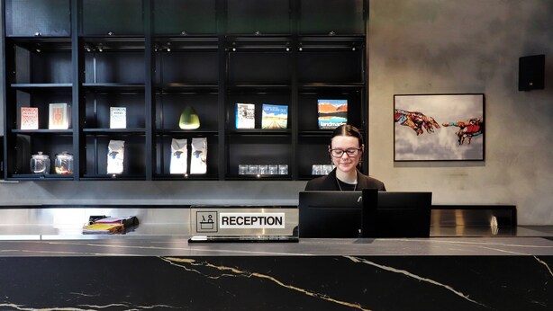 A reception desk with a sign labeled 'RECEPTION' and a person seated behind it. - The Viv Hotel Wellington (Wellington)