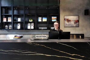 A reception desk with a sign labeled 'RECEPTION' and a person seated behind it. - The Viv Hotel Wellington (Wellington)
