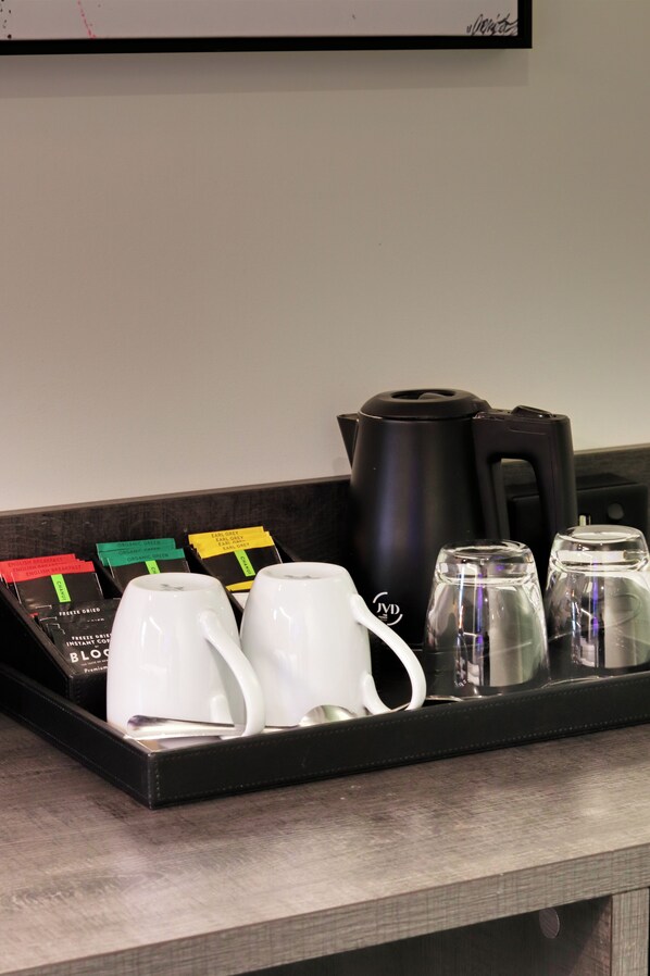 A coffee station with a black coffee pot, two white mugs, and a tray with coffee pods. - The Viv Hotel Wellington (Wellington)