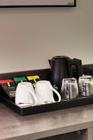 A coffee station with a black coffee pot, two white mugs, and a tray with coffee pods.