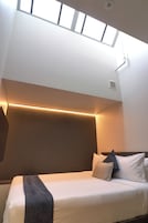 A modern bedroom with a skylight, a bed with multiple pillows, and a bedside table.